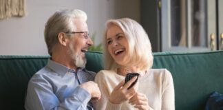 happy retirees family laughing using smartphone home aged husband wife having fun ecommerce shopping watching funny 157924030
