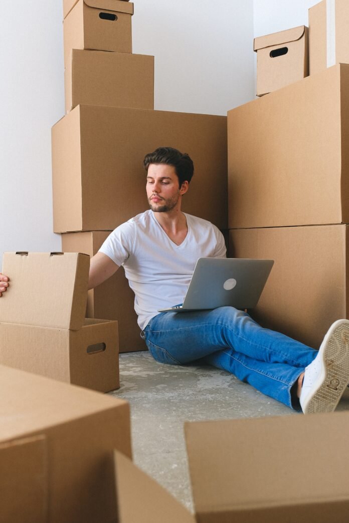 serious young self employed guy using laptop and packing boxes before relocation 1